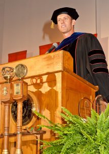 man at podium wearing university regalia giving a speech