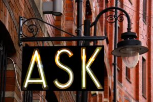 A sign stating, "ASK" next to a lamp post.