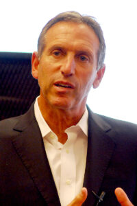 A photograph of Howard Schultz from the navel up. He is wearing a white collared shirt without a tie and a suit jacket.