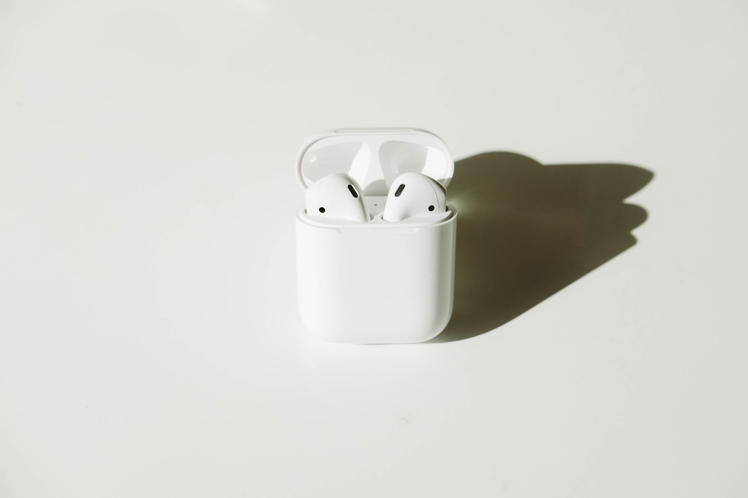 Airpods sit in their case and have a shadow. The picture has a white background.