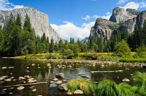 A valley view of Yosemite, with water, grass, trees, and distant peaks.