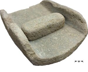 A stone mano is placed on a metate.