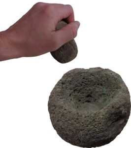 A hand is holding a stone pestle over a mortar.