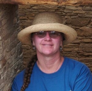 Woman wearing a hat and sunglasses in front of a stone wall.